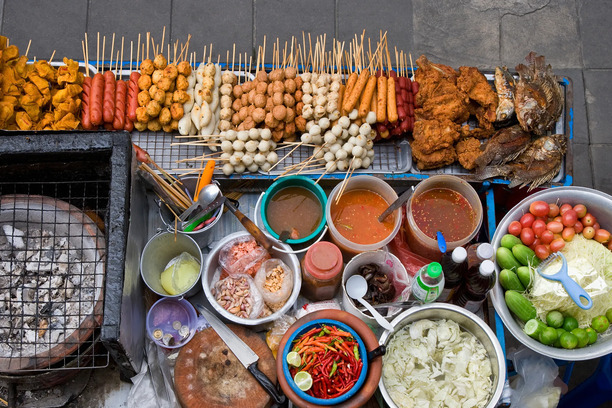 Street food stall on Silom Road in Bangkok serving grilled skewers and som tam (green papaya salad) to locals and tourists.